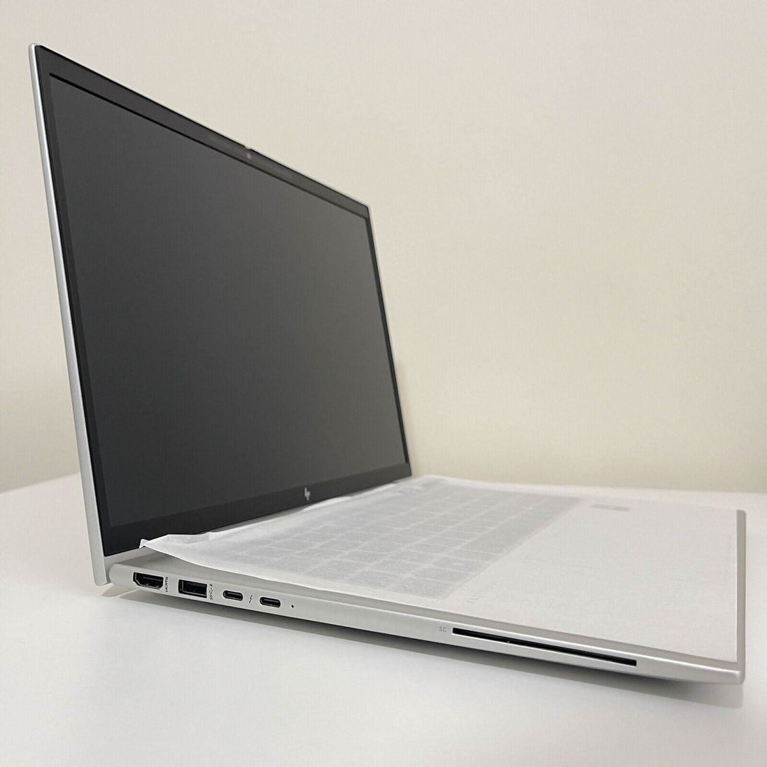 Silver laptop with black screen, side view showing ports, on a white desk