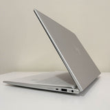 Silver laptop partially open on white desk, slim design, visible ports on side